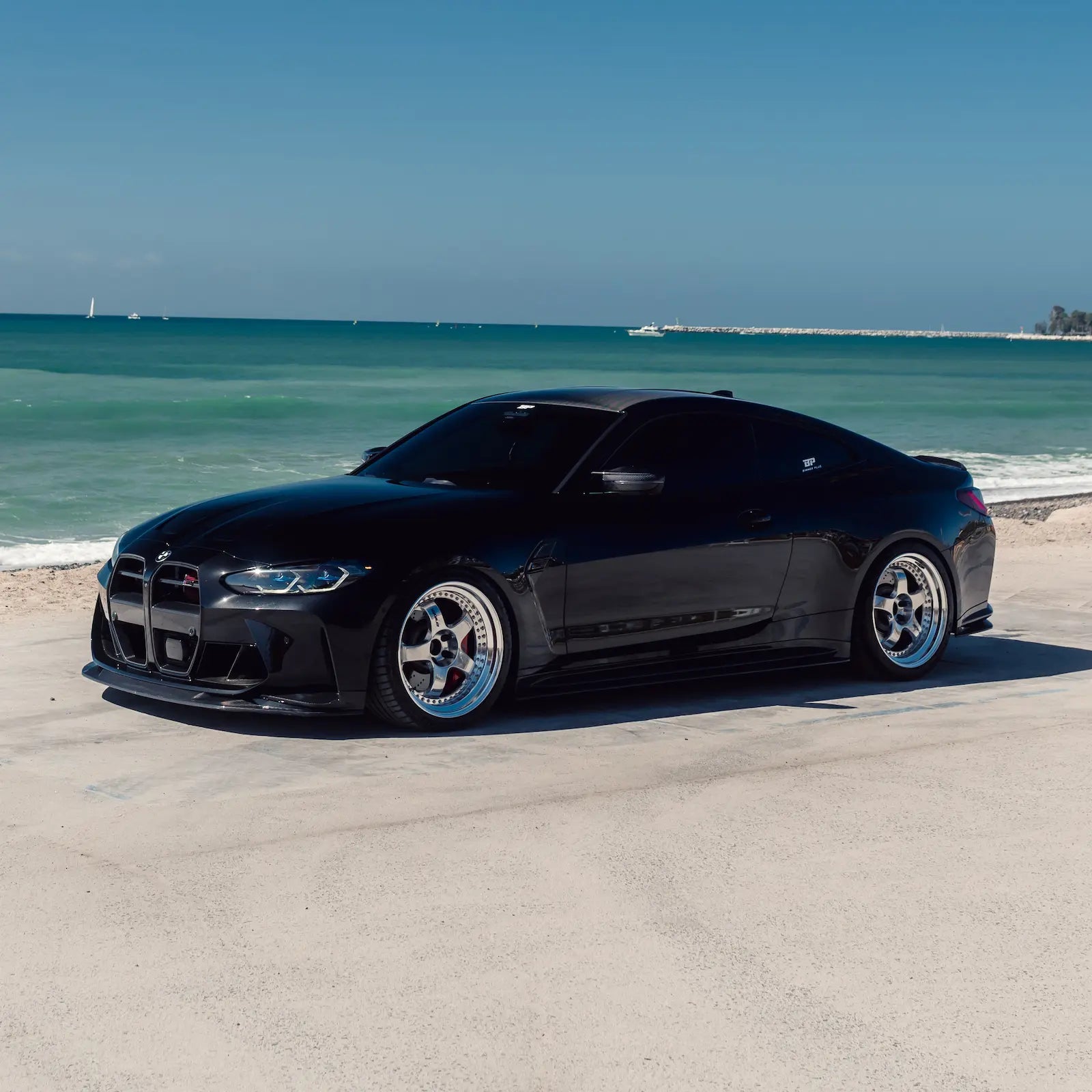 Black BMW G82 M4 on a beach with ocean and sky in the background
