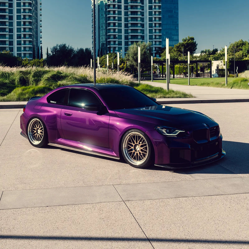 Purple BMW G87 M2 parked on a concrete surface with buildings in the background