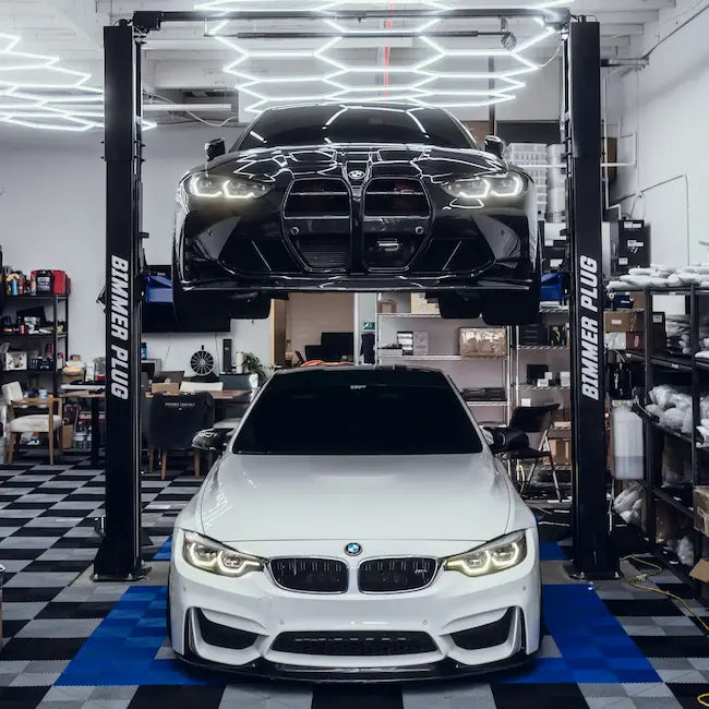 Two BMW cars in the Bimmer Plug Irine garage setting with one on a lift.